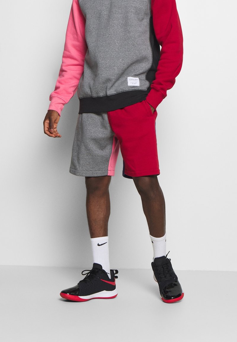 Sweat-shirt à blocs de couleurs gris et rouge avec une manche rose, assorti à un short gris et rouge. Chaussures de sport noires et chaussettes blanches visibles.