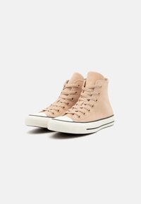 Zapatillas altas beige con cierre de cordones, parte superior texturizada, punta de goma blanca y rayas negras de acento en la suela.