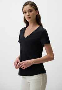 Czarna koszulka z dekoltem w serek, wykonana z gładkiego materiału, z krótkimi rękawami i dopasowanym krojem, noszona z jasnymi spodniami.