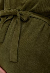 Oliwkowy kordurojowy materiał z przewiązanym paskiem, z pionowymi prążkami i marszczonym wykończeniem w talii.