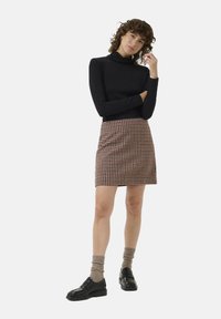 Un haut en col roulé noir associé à une mini jupe à carreaux marron et crème. Le mannequin porte des chaussures noires et des chaussettes beiges côtelées.