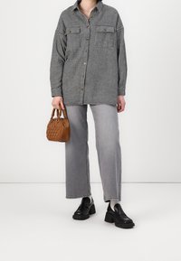 Czarna i biała, w kratę, oversize'owa koszula z dwoma kieszeniami na piersi, zestawiona z szarymi spodniami typu wide-leg i małą brązową torebką. Czarne buty na platformie.