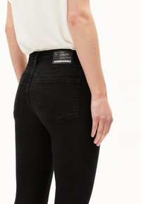 Jeans de mezclilla negra con un diseño ajustado. Cuenta con dos bolsillos traseros y una etiqueta rectangular en la cinturilla. Textura suave.