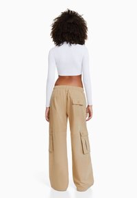 Beige cargobroek met een elastische tailleband, zijzakken en een losse pasvorm, gecombineerd met een witte geribbelde languit top.