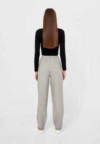 Pantalons taille haute gris clair avec une jambe droite, comportant des poches arrière et des détails de couture subtils. Portés avec un haut noir à manches longues.