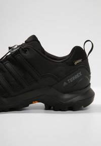 Czarne buty trekkingowe z teksturowanym materiałem górnym, gumową podeszwą i charakterystycznym systemem sznurowania. Posiadają logo GORE-TEX oraz wzmocnioną piętę.