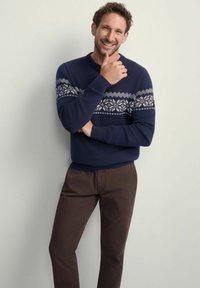 Navy niebieski sweter z dzianiny z białym wzorem opadów śniegu na klatce piersiowej, w połączeniu z brązowymi spodniami. Gładka tekstura, luźny krój.