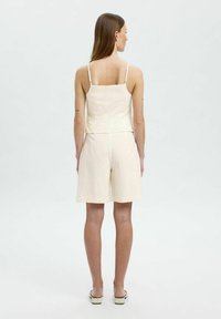 Lys beige linned to-delt outfit bestående af en tætsiddende cami med tynde stropper og løse shorts, tekstureret stof og et enkelt design.