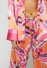Completo loungewear in satin con un motivo astratto arancione, rosa e viola. Include una camicia con bottoni e pantaloni con coulisse, con polsini a contrasto.