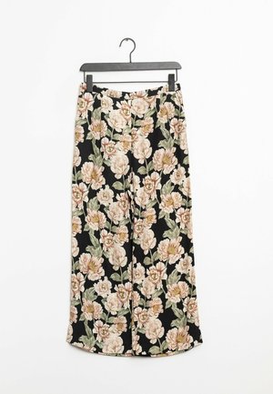 Czarne szerokie spodnie o kwiatowym wzorze w kremowe i zielone kolory wiszą na czarnym wieszaku na białym tle.