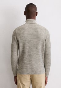 Hellgrauer gerippter Rollkragenpullover mit langen Ärmeln, strukturiertem Stoff und figurbetontem Design. Getragen mit beigen Cordhosen.