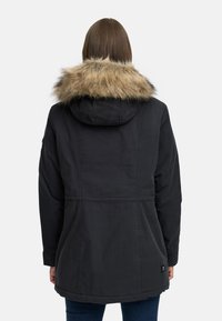 Melna parka jaka ar mākslīgās kažokādas odere ap kaklu, ar sašaurinātu vidukli, garām piedurknēm un gludu tekstūru. Parādīta aizmugures skata.