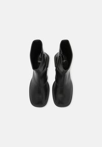 Bottes cheville en cuir noir à finition lisse, bout carré, et fermetures éclair latérales, présentant un design élégant et une semelle plate en caoutchouc.