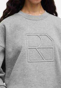 Sweatshirt grigio realizzato in morbido materiale, caratterizzato da un logo geometrico in rilievo di una tonalità più scura. Collo tondo ordinato e polsini a costine.