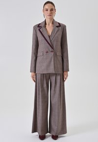 Gecontroleerde blazer en brede broek, bruin met bordeaux accent. Heeft een notch kraag, dubbele knopen en voorzakken.