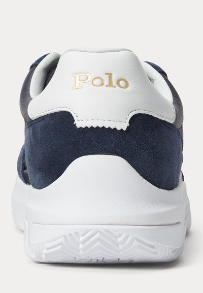 Tengerészkék velúr sportcipő fehér bőr sarokkal, arany "Polo" logóval és texturált gumitalppal, amely cikkcakk mintát kínál a tapadás érdekében.