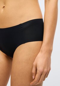 Juodos spalvos bikinio kelnaitės, pasižyminčios lygiu audiniu, elastinga juosmens juosta ir minimalistiniu dizainu. Artimas aprangos šono ir juosmens vaizdas.