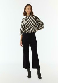 Gestreepte blouse in zwart en beige met een ronde halslijn en pofmouwen, gecombineerd met zwarte ankle-length broek en grijskleurige puntige laarzen.