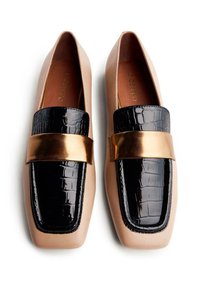 Mocassins beige clair avec un bout noir en motif crocodile brillant et une bande métallique dorée sur le dessus. Texture lisse sur l'ensemble.