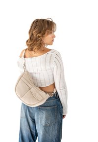 Borsa a tracolla color beige con imbottitura, dalla forma arrotondata, tasca con zip e tracolla regolabile. Indossata sopra un crop top bianco a coste e jeans in denim.