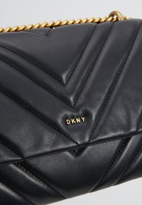 Sac à main en cuir noir matelassé avec bandoulière chaîne dorée et petit logo DKNY doré sur le rabat avant.
