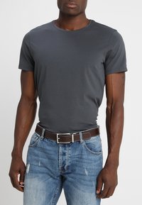 Dunkelgraues T-Shirt mit kurzen Ärmeln, kombiniert mit hellblauen, distressed Jeans und einem braunen Leder Gürtel mit einer silbernen Schnalle. Minimalistisches Design.