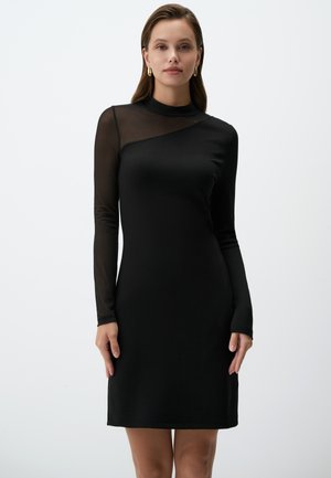 Robe noire avec de longues manches en maille transparente et un col montant. Tissu lisse, forme ajustée et détail de décolleté asymétrique. Design simple.