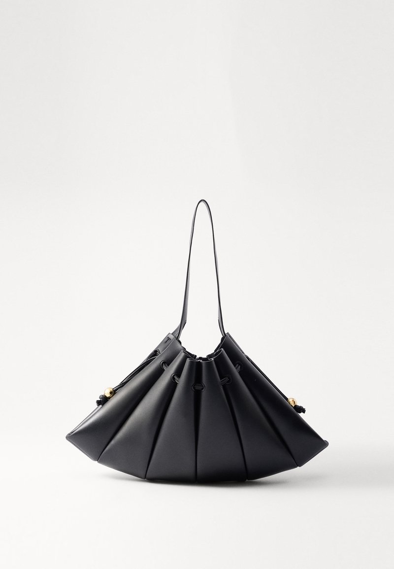 Svart plisserad handväska i slät läder, med ett enda handtag, guldaccenter och en geometriskt strukturerad form.