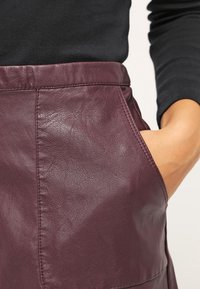 Burgundy nahkan hame, jossa on litteä vyötärö, sivutasku ja sileä pinta, jossa on näkyviä ompelutietoja.