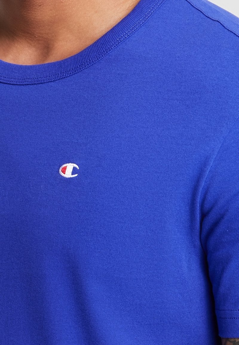 T-shirt in cotone blu con collo a giro e maniche corte, con un piccolo logo ricamato in bianco e rosso sul petto.