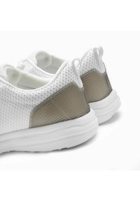 Weiße Mesh-Sneaker mit einem strukturierten, halbtransparenten Rückeneinsatz und einer gepolsterten, weißen Gummisohle. Sicherer Sitz mit Fersenlasche.