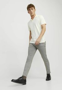 Polo shirt beige con colletto e maniche corte, pantaloni grigi chiari su misura e scarpe nere con lacci. Tessuto liscio con una vestibilità pulita e moderna.