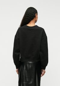 Μαύρη φούτερ με χαλαρή εφαρμογή, ρίγες στους ώμους, ραμμένα μανίκια και στρίφωμα; φορεμένη με μια μαύρη δερμάτινη φούστα; λεία υφή.