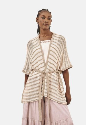 Cárdigan de punto beige con frente abierto, rayas horizontales, mangas cortas y un cinturón a juego; llevado sobre una blusa clara y una falda de capas.