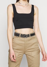 Svart kort topp med fyrkantig halsringning. Bärs med beiga cargobyxor som har fickor i lappar och ett svart bälte med silverdetaljer.