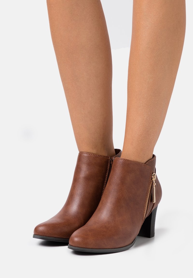 Bottes bottines en cuir synthétique marron avec un bout arrondi et une fermeture éclair latérale. Elles possèdent un talon épais de 3 pouces et une texture lisse.