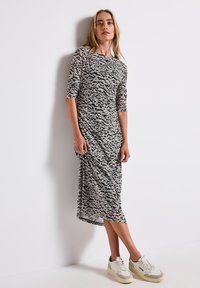 Schwarz-weiß gemustertes Midi-Kleid mit Dreiviertelärmeln, aus weichem Stoff, kombiniert mit weißen und beigen Turnschuhen.