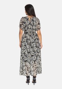 Robe maxi noire à motif floral, avec des manches courtes flottantes, une taille cintrée et un détail dos en forme de clé. Elle se compose d'un tissu transparent avec des accents crème et or.
