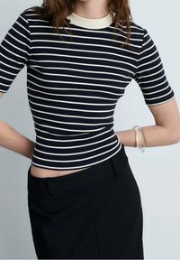 Námořnická a smetanová pruhovaná krátkosrstá blůza s přiléhavým střihem a kulatým výstřihem, zkombinovaná s černou sukní s jemným proužkem.