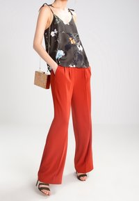 Czarna, kwiecista jedwabna bluzka z wiązanymi ramiączkami, zestawiona z szerokimi, wysokimi spodniami w kolorze czerwonym. Czarne sandały na obcasie oraz kwadratowa, pleciona torebka dopełniają całość.