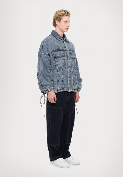 Jachetă din denim cu o croială lejeră, având două buzunare frontale, guler răspândit și bisturiu cu șnur. Asortată cu pantaloni închisi la culoare și teniși albi.