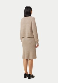 Beige ribbad stickad tröja och kjol set, som har en kortad tröja och en kjol i medellängd, med långa ärmar och en avslappnad passform. Svarta klackskor med blockklack.