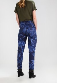 Blå kamouflagemönstrade byxor med tapered passform, med medelhög midja och bakfickor, i kombination med svarta klacksneakers.