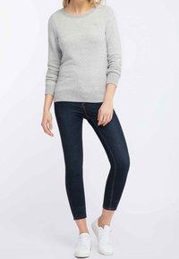 Sweat-shirt gris clair à col rond, poignets et ourlet côtelés. Jean skinny bleu foncé avec une coupe ajustée. Des baskets blanches complètent le look.