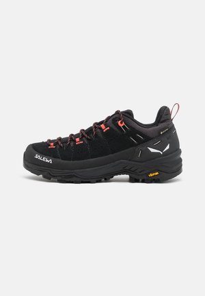 Black hiking shoes with a suede and textile upper, featuring red accents, a rugged rubber outsole, and visible perforation for breathability.