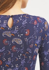 Laivastonsininen mekko kukkakuviolla, jossa on avainreikäleikkaus selässä ja pyöreä musta nappisuljin. Pehmeä, teksturoitu kangas.