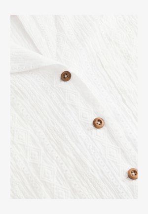 Bjela teksturirana tkanina s dijamantnim uzorkom i tri smeđa gumba. Materijal izgleda lagano i blago uzorkovano.