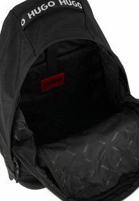 Mochila negra hecha de nailon con una parte superior redondeada. El interior presenta un forro de marca, cierre de cremallera y un logo prominente en la correa.