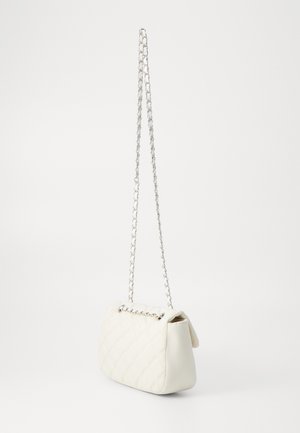 Petit sac à main blanc matelassé avec une bandoulière chaîne argentée suspendu sur un fond blanc uni.