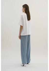 Hvid oversized t-shirt med korte ærmer, parret med lyseblå vide bukser, der viser glat stof og en afslappet pasform.